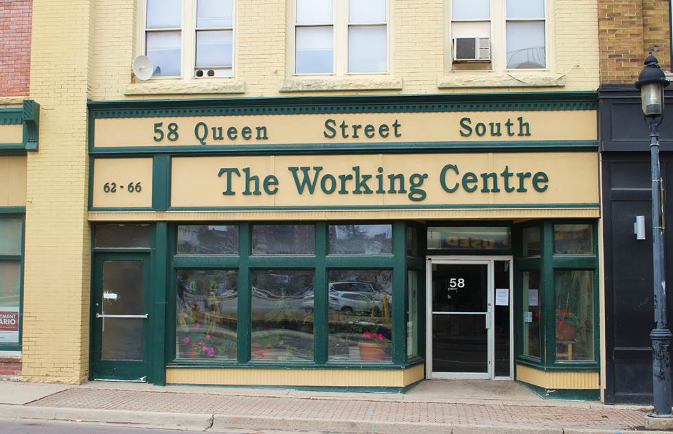 The 58 Queen South building has a tan coloured facade with green trim and window framing. A glass door with metal framing is the entrance to the Job Search Resource Centre.