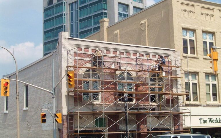 Workers stand on scaffolding to revitalize the brick facade of the building at 66 Queen Street South.