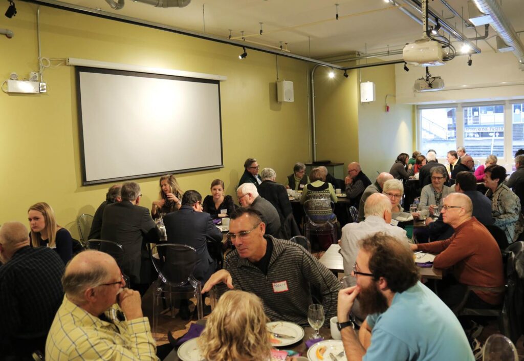 A full crowd of people sit at tables talking inside the Fresh Ground space.