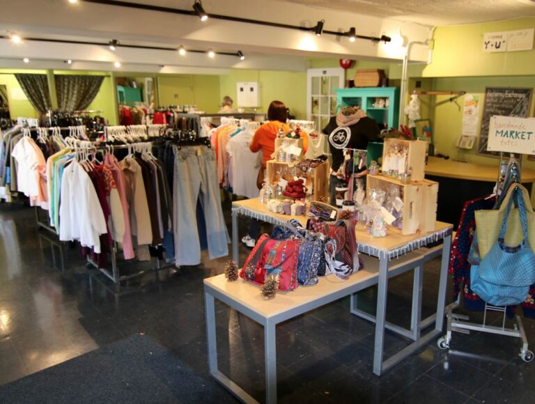 People browse clothing racks inside the former Green Door thrift shop. Tables in the foreground displays various products and items.