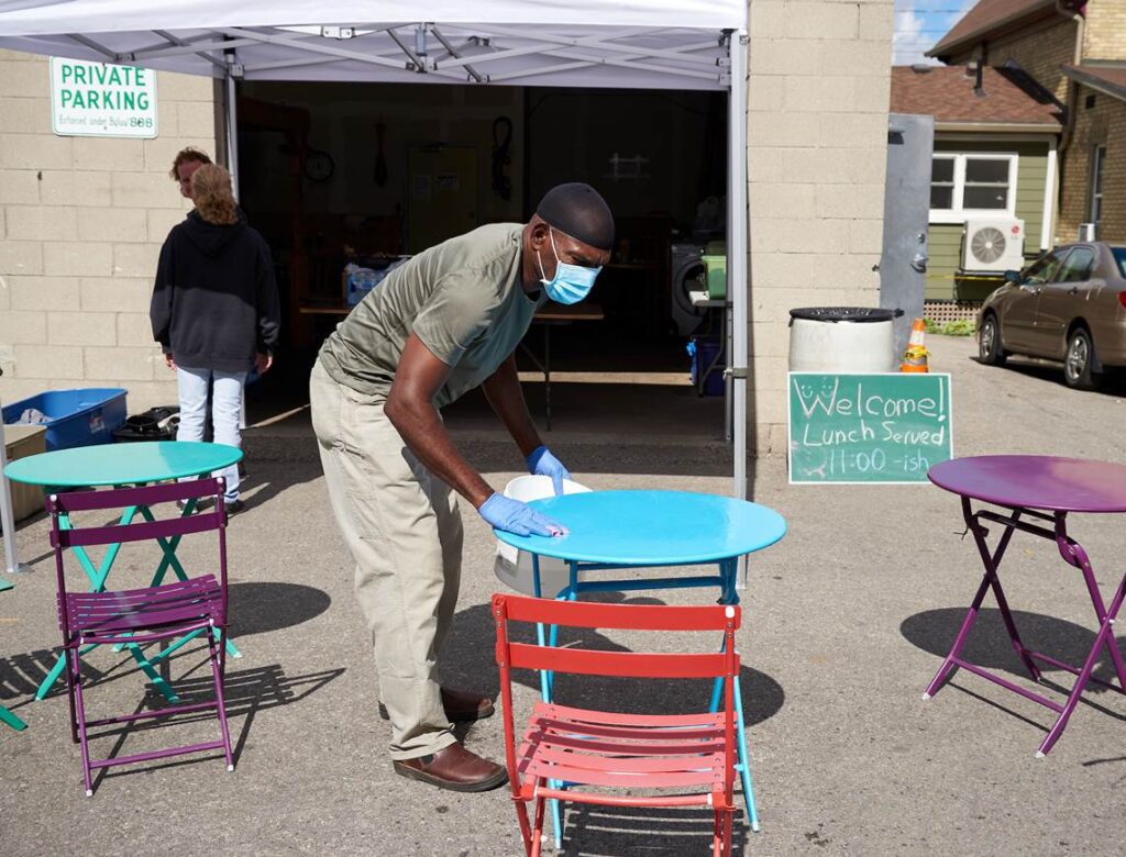 During the pandemic, a worker wearing a face mask cleans a blue table outside Saint John's Kitchen before the daily meal is served.