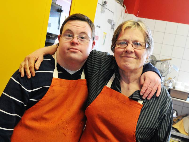 Saint John's Kitchen workers wearing dark shirts and orange aprons embrace with arms around each other