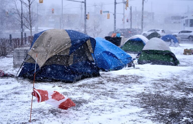 A group of encampment tents sit outside during a windy snow storm