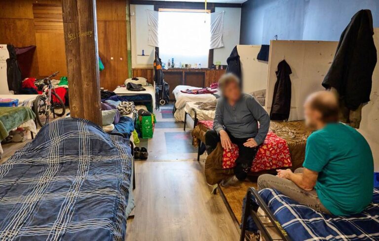 Two residents sitting on beds talk to one another inside King Street Shelter