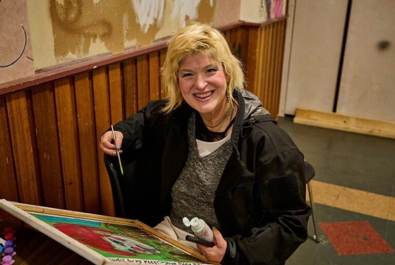 A resident of King Street Shelter poses for a photo while painting a piece of art