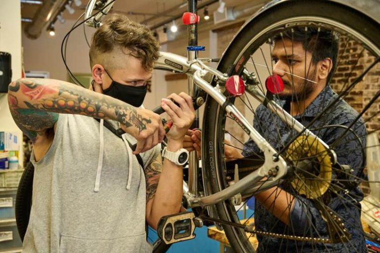 A man with a tool works on a bicycle inside the Recycle Cycles shop